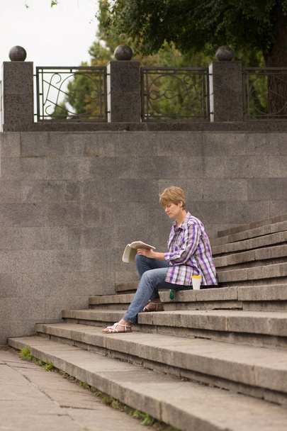 positive Frau sitzt und liest ein Buch auf den Stufen - Foto, Bild