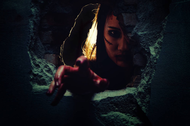 Horrorszene mit blutiger Hand des Bösen kommt aus einem dunklen Loch. Halloween-Konzept. Fokus auf Gesicht. - Foto, Bild