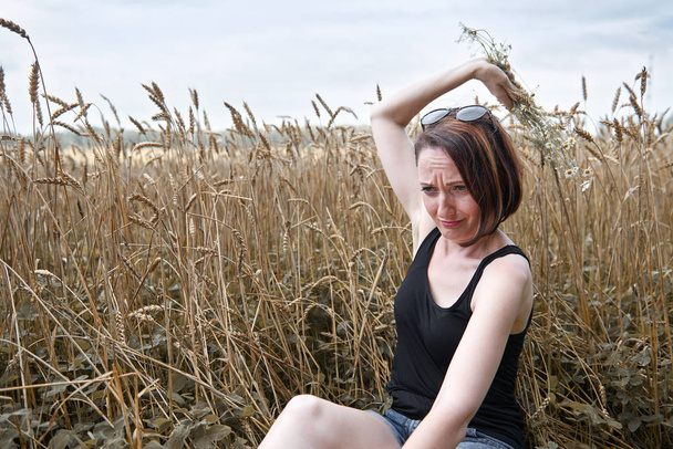 mladá dívka s kyticí sedí poblíž pšeničné pole. Si vybírá z okvětních lístků a zajímá Vás, k milovat nebo nemilovat, staré lidové legendy a tradice. - Fotografie, Obrázek