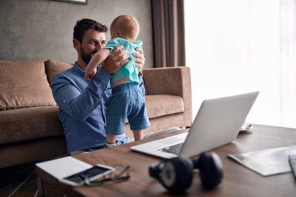 Smiling man working from home and taking care of baby - Fotoğraf, Görsel