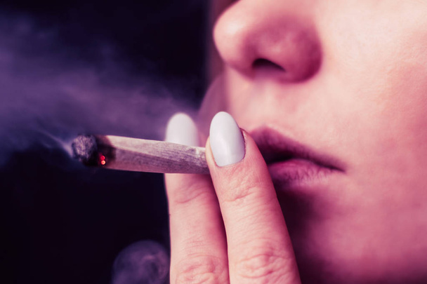Cannabis-Unkraut, ein Joint in seinen Händen Eine Frau raucht. Rauch auf schwarzem Hintergrund. Konzepte des medizinischen Marihuana-Konsums und der Legalisierung von Cannabis. Auf schwarzem Hintergrund rosa Tönung - Foto, Bild