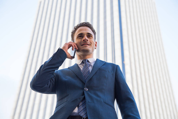 Allegro uomo d'affari elegante indossa abito formale e avere conversazione telefonica in posa su sfondo urbano
. - Foto, immagini