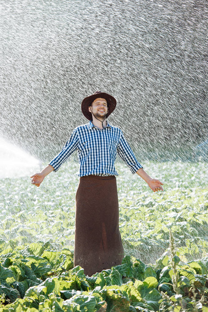 A mezőgazdasági termelő a kalapban élvezi az eső. A fiatalember vizesek alatt az eső nyáron. - Fotó, kép