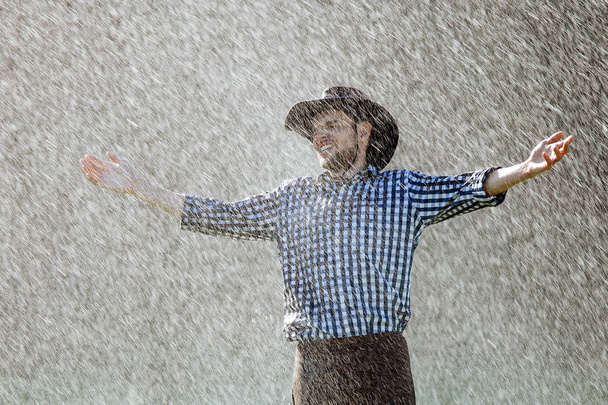 Der Bauer mit dem Hut genießt den Regen. Junger Mann wird im Sommer nass unter dem Regen. - Foto, Bild
