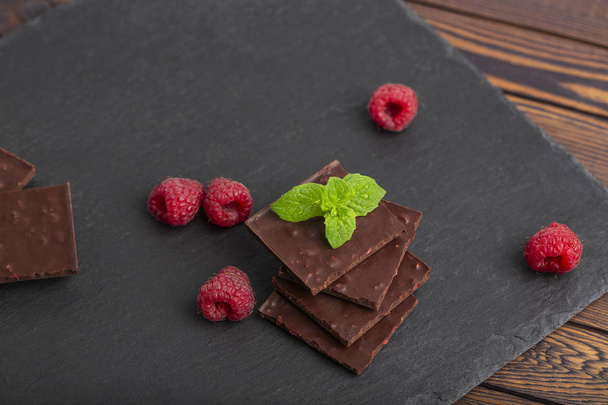 Шоколад с кусочками сухой малины и свежей малины с мятным листом на тарелке. Закрыть
. - Фото, изображение