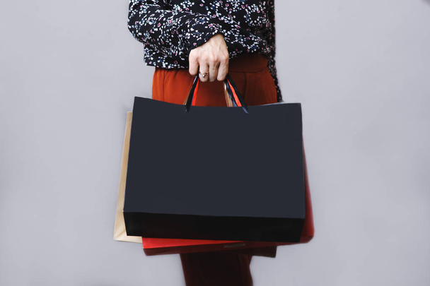 Crop side view of woman in blouse and terracotta trousers standing with paper shopping bags in hand isolated on gray background - Foto, Bild