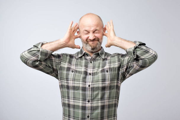 Geërgerd volwassen man inpluggen oren met vingers. Ik wil niet te horen van deze roddels - Foto, afbeelding
