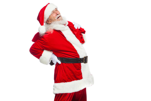 Christmas. Santa Claus is suffering from back pain and holds a red bag with gifts on his back. Isolated on white background. - Foto, imagen