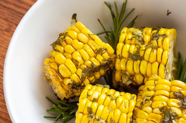Cooked in the oven corn with herbs on a wooden background in white bowl closeup, top view - Foto, afbeelding