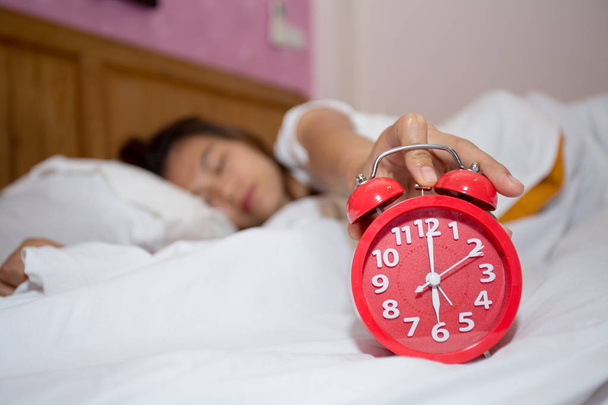  Годинник тривоги в спальні з ледачою жінкою спить намагаючись зупинити відкладення. Ранкова концепція, безсоння спить, турбуються і підкреслюють концепції
 - Фото, зображення