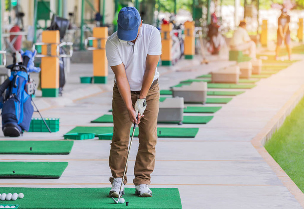 golfaaja metalli golfmailalla valmistautuu ajamaan golfpalloa harjoituksen aikana ampumaradalla golfkentän piha merkkejä
 - Valokuva, kuva