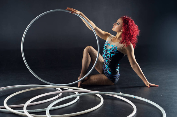 Hula-hoop girl performs circus performer in an artistic costume. Studio shooting on a dark background. - Foto, Imagem