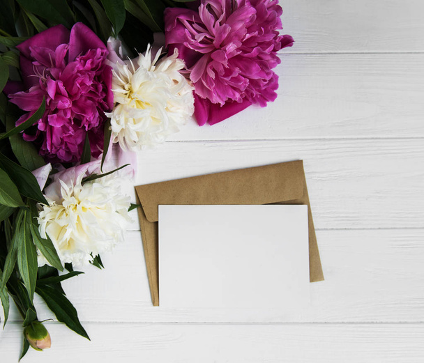 cartão de convite, envelope de artesanato e flores de peônia rosa em um fundo de madeira branca
 - Foto, Imagem