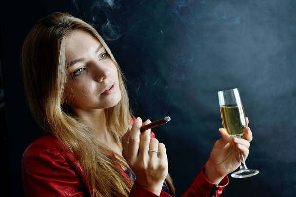 Jovem fêmea senta-se com cigarro e um copo de vinho branco na mão. Mulher de casaco vermelho
. - Foto, Imagem