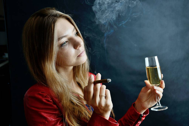 Jonge vrouw zit met cigarillo en glas witte wijn in haar hand. Vrouw in rode jas. - Foto, afbeelding