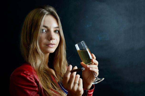 Young female sits with cigarillo and glass of white wine in her hand. Woman in red jacket. - Photo, Image