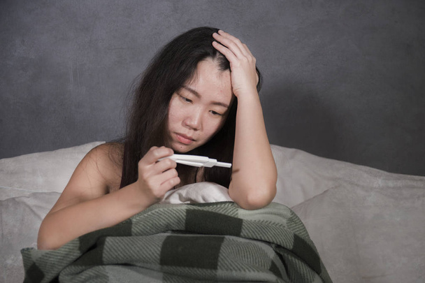young depressed and desperate Asian Korean woman crying and scared testing positive result on pregnancy test alone in bed feeling remorse and stress in irresponsible mistake concept - Valokuva, kuva