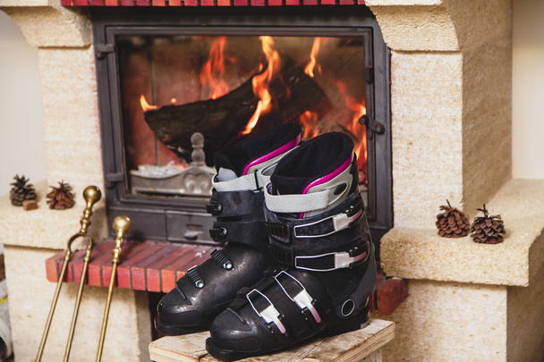 Séchage des chaussures devant la cheminée. Deux chaussures de ski se tiennent sur un tabouret devant un foyer allumé
 - Photo, image
