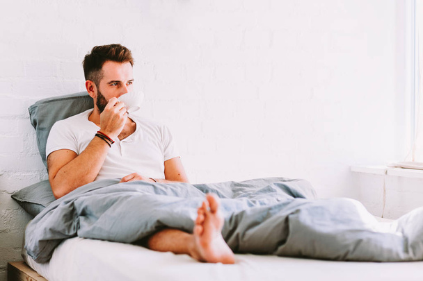 Young man drinking coffee in bed - Photo, Image