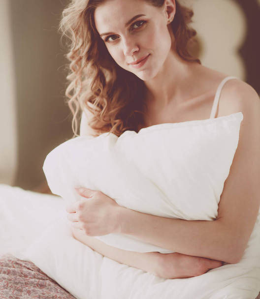 Young woman holding a pillow while sitting on her bed. - Foto, imagen