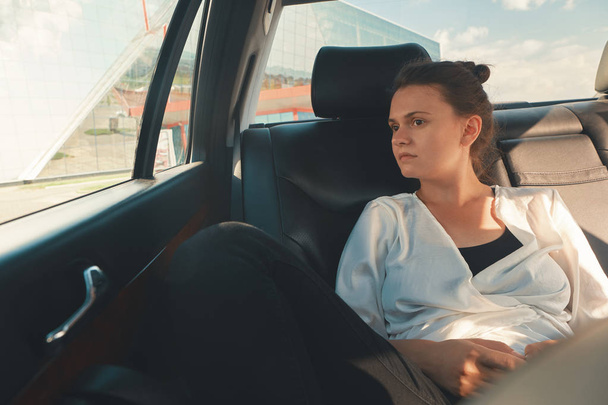 Mujer moderna sentada en el asiento trasero del coche en viaje por carretera Relajante
 - Foto, Imagen