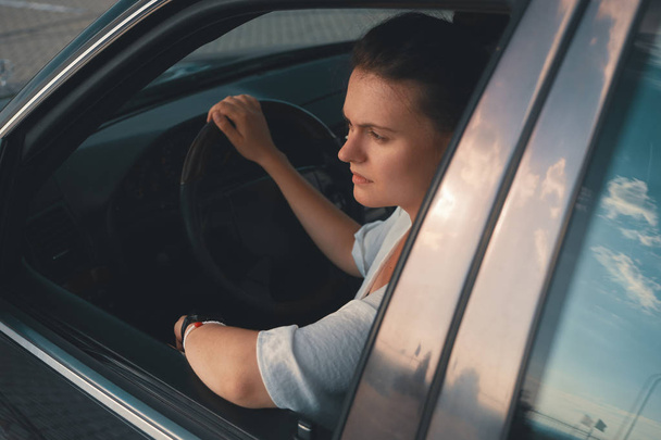Vista di attraente giovane donna in abbigliamento casual mettere la testa fuori dal finestrino durante la guida di una macchina. Fiducioso e bello
.  - Foto, immagini