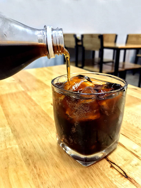 Cola in ghiaccio di vetro, Versare cola da bottiglie di vetro bevande a un bicchiere con cubetti di ghiaccio, cola in bevanda di ghiaccio di vetro Bevande sul tavolo del ristorante
 - Foto, immagini