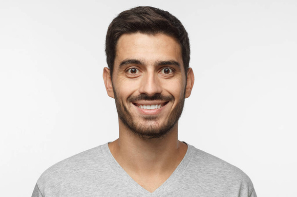 Close up portrait of smiling handsome man in gray t-shirt isolated on gray background - Foto, afbeelding