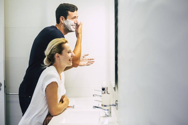 mooie jonge man doen en snijden baard met spons terwijl vrouw lachen  - Foto, afbeelding