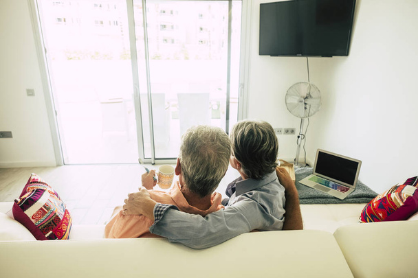 вид ззаду старшої пари сидить вдома на білому дивані і п'є чай
 - Фото, зображення