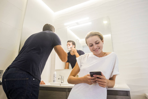 Sarışın genç kadın smartphone sakal köpüklü banyo yapıyor adam bakıyor  - Fotoğraf, Görsel