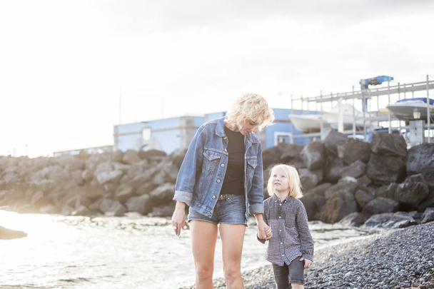 young beautiful blonde salope mother and son woman and boy people walking on the shore at the beach during vacation or outdoor sea leisure activity - Photo, image