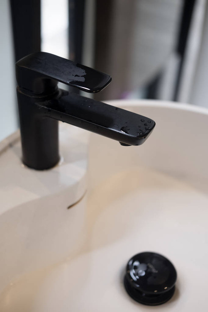 Zamknąć na wody spada z nowoczesnych czarny kranu do klasycznego biała umywalka - Zdjęcie, obraz