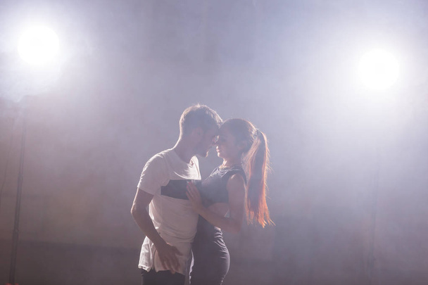 Dançarinos habilidosos se apresentando na sala escura sob a luz do concerto e fumaça. Casal sensual realizando uma dança contemporânea artística e emocional
 - Foto, Imagem