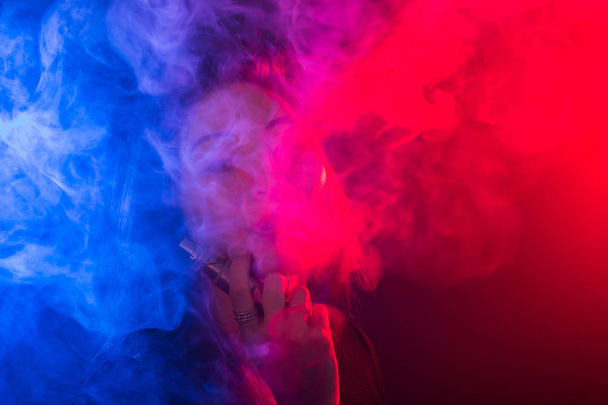 Young woman smoking vape or e-cigarette in neon light - 写真・画像