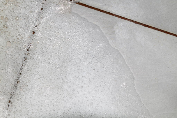 Detergente de sabão de bolhas com esfregar a sujeira do chão do banheiro molhado, espuma bolha branca de lavagem de shampoo na vista superior do chão Tiled
 - Foto, Imagem