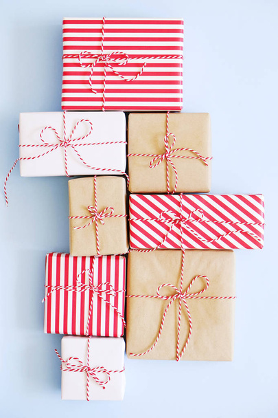 Viele Weihnachtsgeschenke sind in rotes, weißes und Bastelpapier verpackt, das mit einem Bindfaden vom Bäcker gebunden ist. mehrere Neujahrsgeschenke in verschiedenen Verpackungen. Draufsicht, Nahaufnahme, Kopierraum, Hintergrund, flache Lage. - Foto, Bild