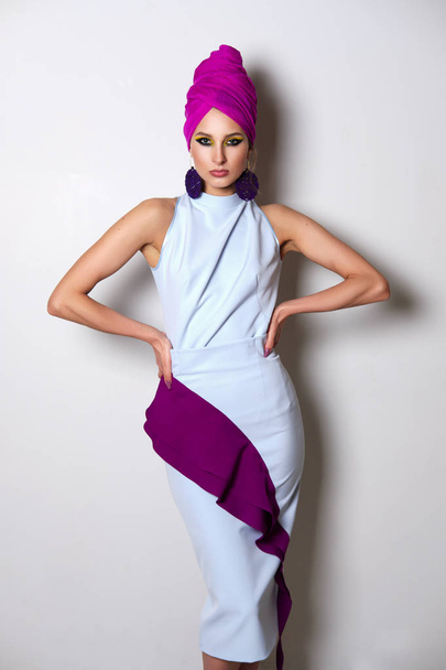 Portrait of beautiful fashion model in fitted dress and turban on head. Bright makeup and big earrings - Фото, изображение