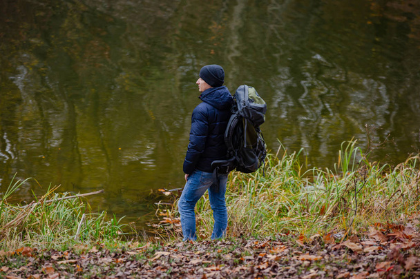 viajero está de pie con una mochila sobre sus hombros en la orilla en el fondo de un lago en el otoño
 - Foto, imagen