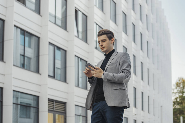 Distant plan of young businessman talking by mobile phone next to skyscraper. - 写真・画像