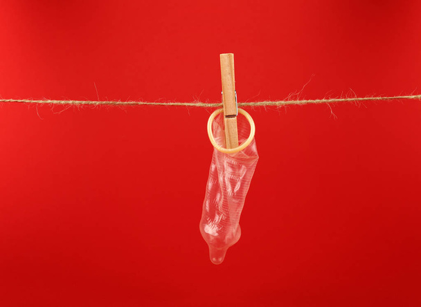 Close up one condom hanging on twine washing line with wooden clothespin over red background with copy space, low angle side view - Fotografie, Obrázek