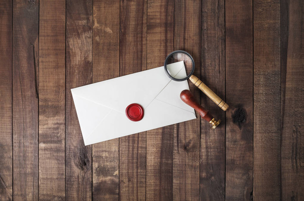 Blank paper envelope with wax seal, stamp and magnifier on wood table background. Mockup for your design. Flat lay. - Photo, Image