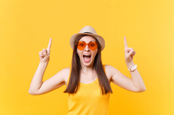 Portrét usměvavé mladé ženy v slaměné Letní klobouk, oranžové brýle zvýrazňující ukazováčků na Kopírovat prostor izolovaných na žlutém pozadí. Lidé upřímné emoce, stylu života. Reklamní plocha - Fotografie, Obrázek