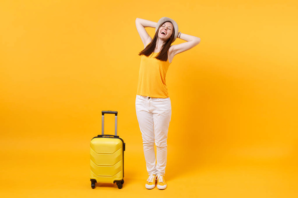 Путешественница туристическая женщина в летней повседневной одежде, шляпа с чемоданом изолированы на желтом оранжевом фоне. Пассажирка, выезжающая за границу на выходные. Концепция полета
 - Фото, изображение