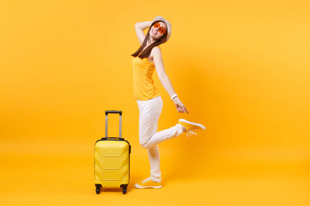 Touristin in sommerlicher Freizeitkleidung, Hut mit Koffer auf gelb-orangefarbenem Hintergrund. Passagierin, die ins Ausland reist, um am Wochenende zu reisen. Flugreise-Konzept - Foto, Bild