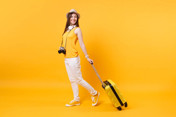 Ταξιδιώτης τουριστικά γυναίκα στο καλοκαίρι casual ρούχα, καπέλο με ακουστικά στο λαιμό που απομονώνονται σε κίτρινο πορτοκαλί φόντο. Επιβάτης που ταξιδεύει στο εξωτερικό για να ταξιδέψετε σε φυγή τα Σαββατοκύριακα. Έννοια του αέρα πτήσης ταξιδιού - Φωτογραφία, εικόνα