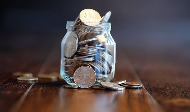 Coins in a glass jar on a wooden floor. Pocket savings from coin - Foto, afbeelding