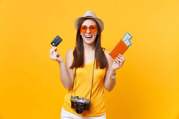 Happy tourist woman in summer casual clothes, hat holding credit card, passport tickets isolated on yellow orange background. Female traveling abroad to travel on weekends getaway. Air flight concept - Foto, afbeelding