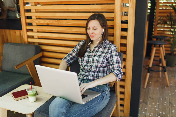 Kadın rahat kıyafetler içinde oturan, modern dizüstü pc bilgisayar üzerinde çalışma, serbest zaman sırasında rahatlatıcı açık havada sokak yaz kahve dükkanı ahşap Cafe. Mobil ofis. Yaşam tarzı serbest iş kavramı - Fotoğraf, Görsel