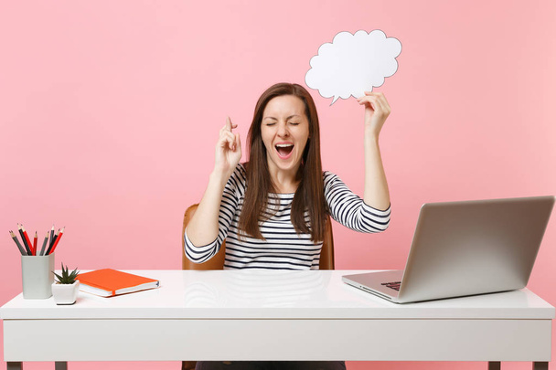 Happy woman wait for special moment keeping fingers crossed hold empty blank Say cloud speech bubble work at office with pc laptop isolated on pink background. Achievement business career. Copy space - Photo, Image